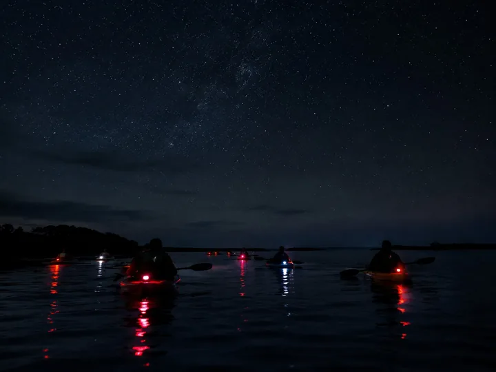 A group of kayaks with small lights in a dark lagoon