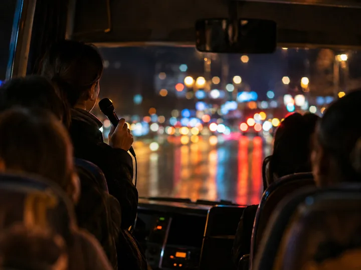 A guide's hand holding a microphone on a bus at night