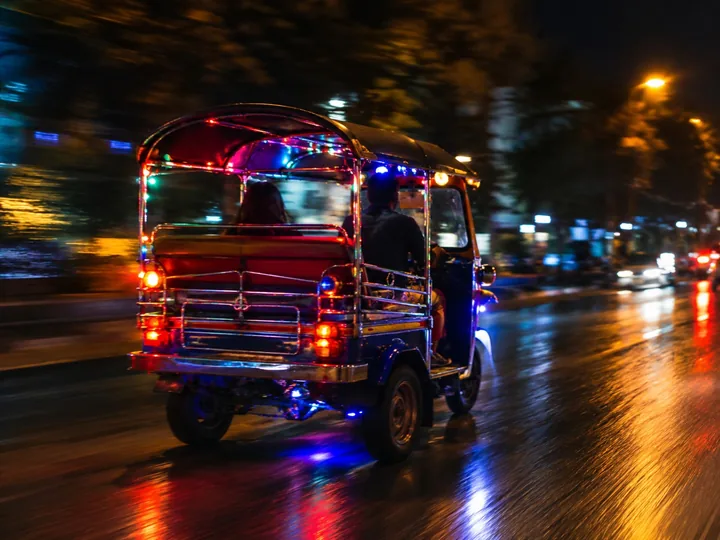 A tuk-tuk with colored lights on a street at night