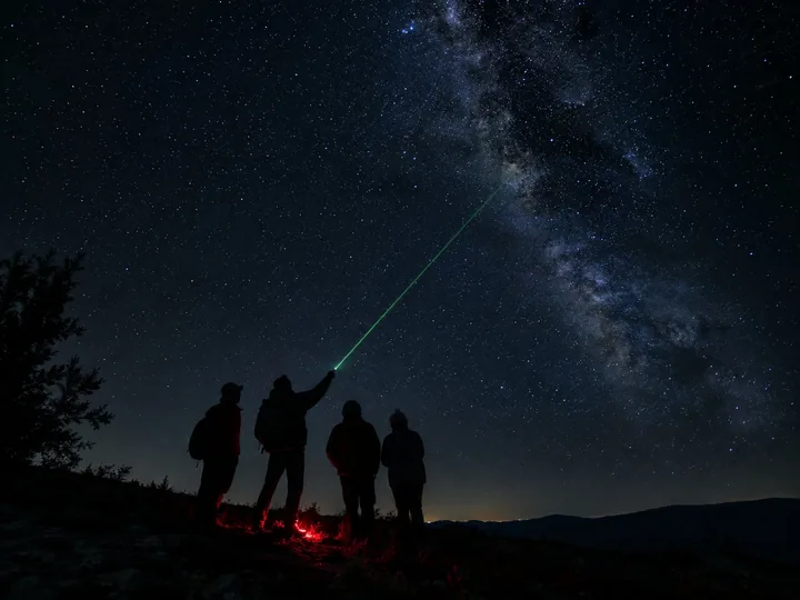 A group silhouetted under the stars with a green laser pointer