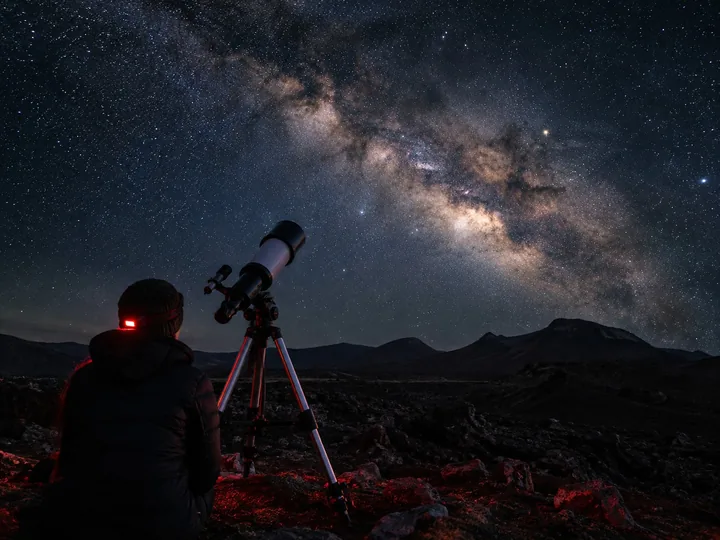 A telescope under the Milky Way in a volcanic landscape