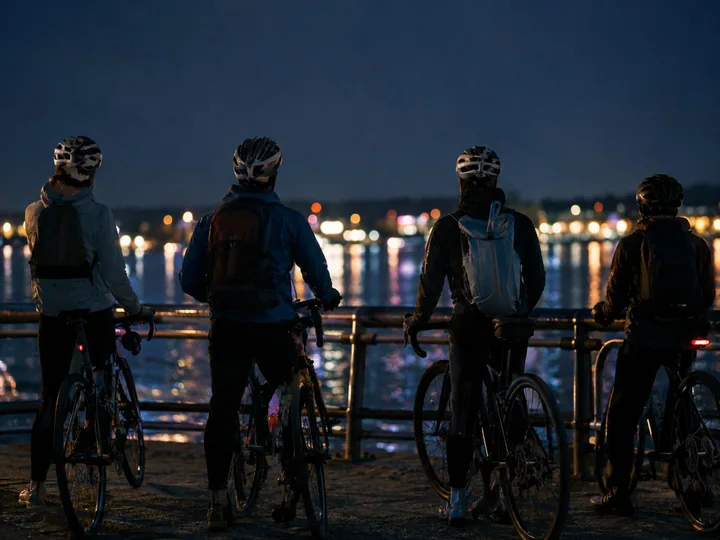 Cyclists stopped together by a lit waterfront at night