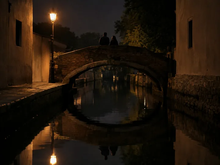 A small stone footbridge over a narrow canal at night