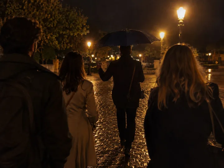 A small group following a guide across a square at night
