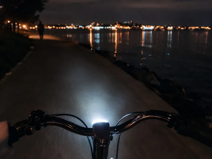 A bike handlebar with a light on a waterfront at night