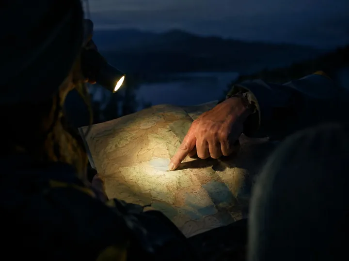 A guide's hand pointing at an old map by flashlight