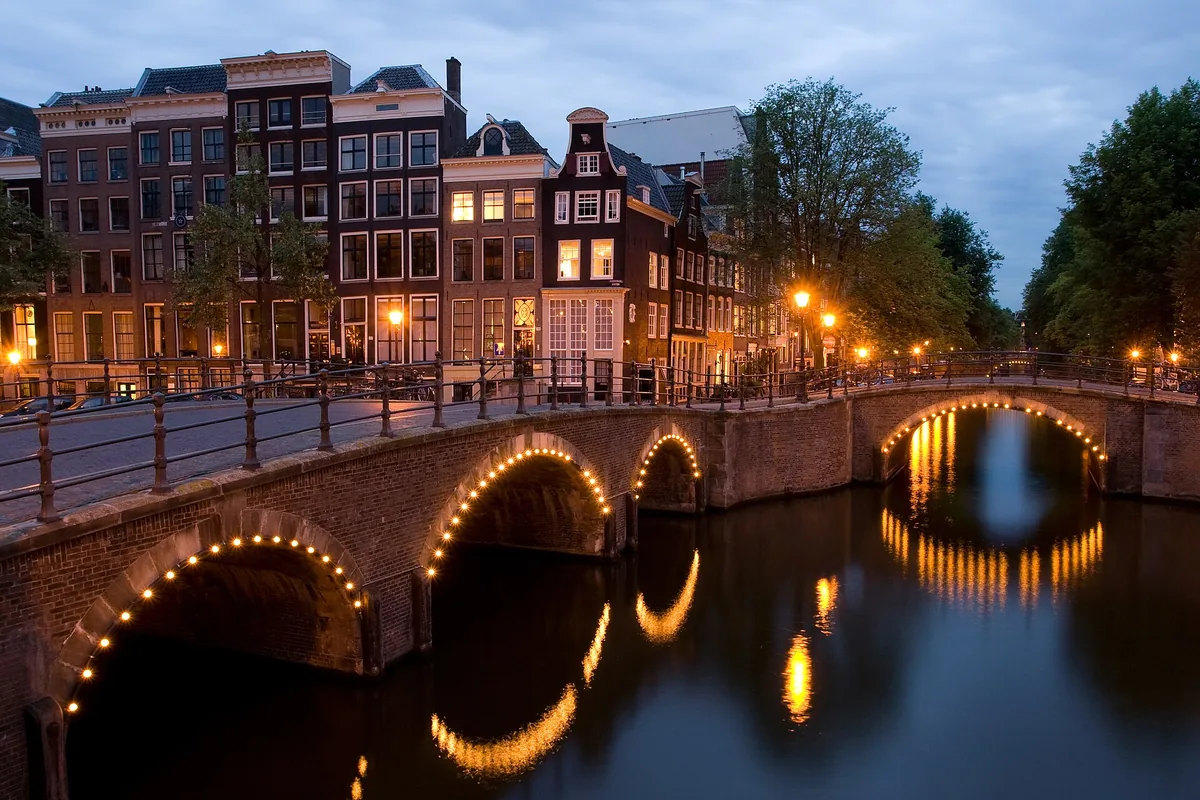 Lit arched bridges over the Reguliersgracht canal in Amsterdam at dusk