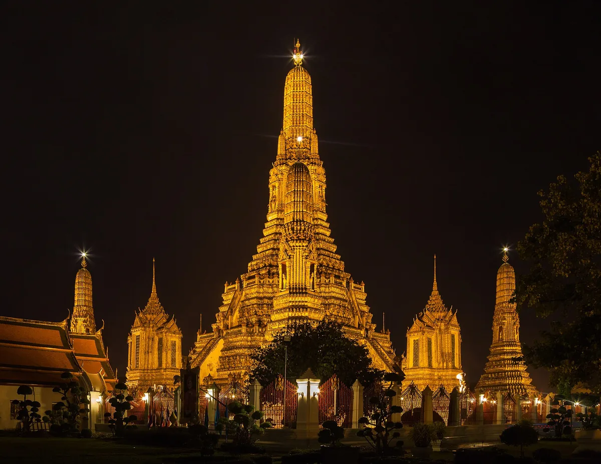 Wat Arun temple in Bangkok floodlit gold against a black night sky