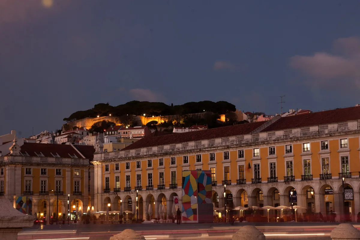 The arcades of Praça do Comércio in Lisbon at dusk, with the castle hill behind