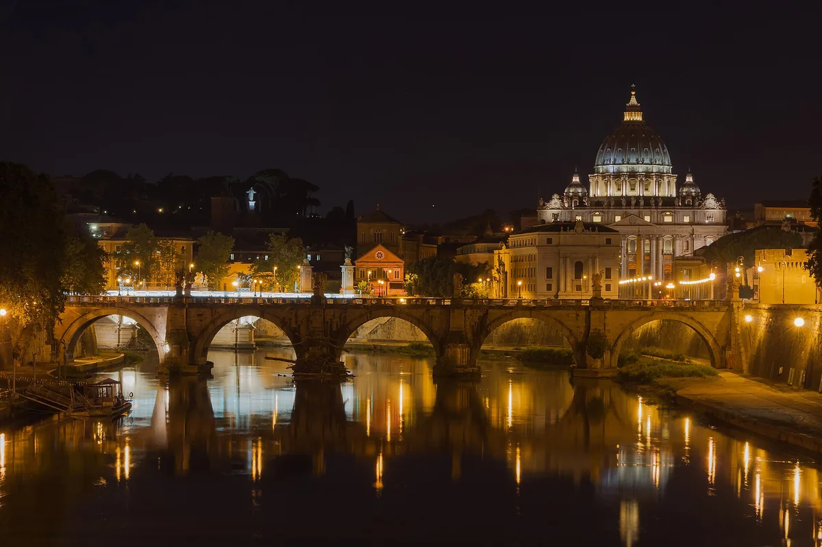 Ponte Sant'Angelo over the Tiber at night, with St. Peter's dome lit behind it