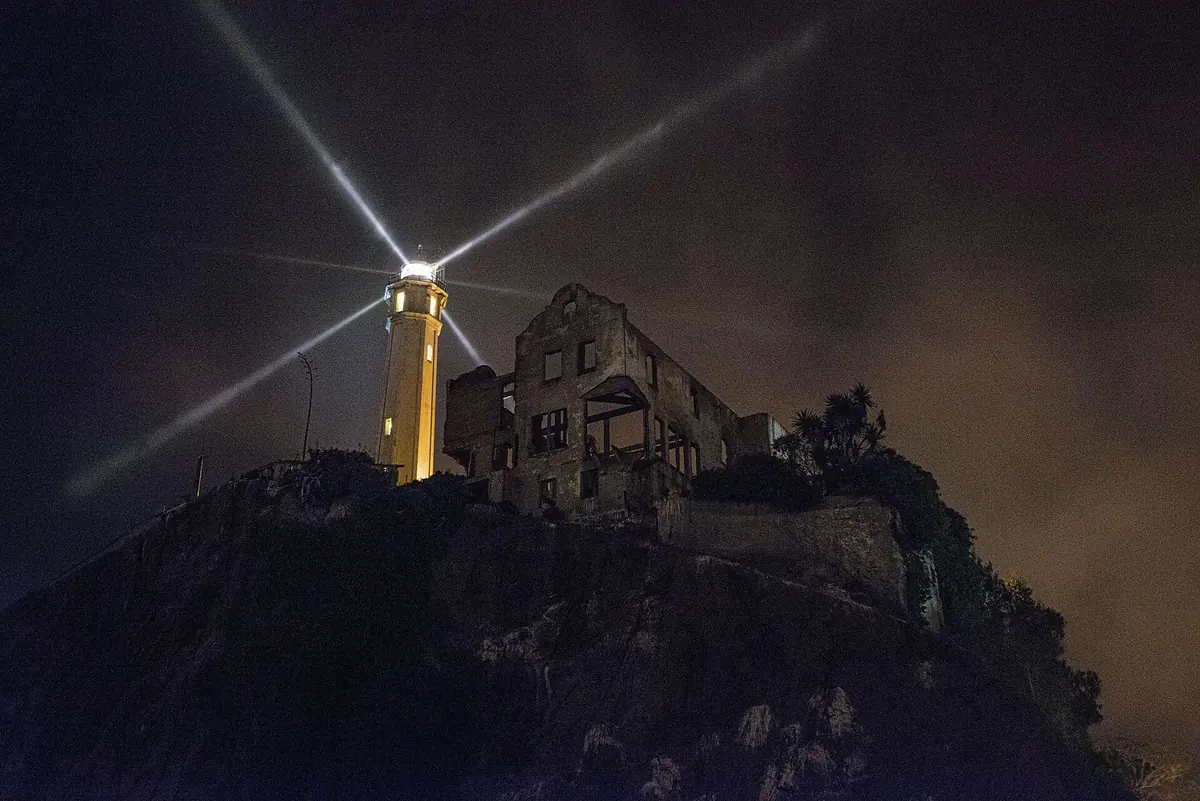 The Alcatraz lighthouse beam sweeping the sky over the island at night