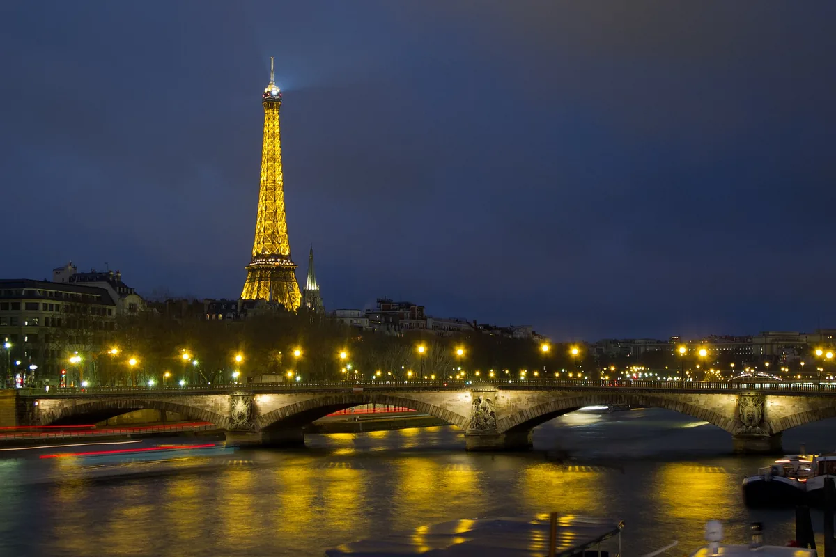 The Eiffel Tower lit gold above the Seine and the Pont des Invalides at night
