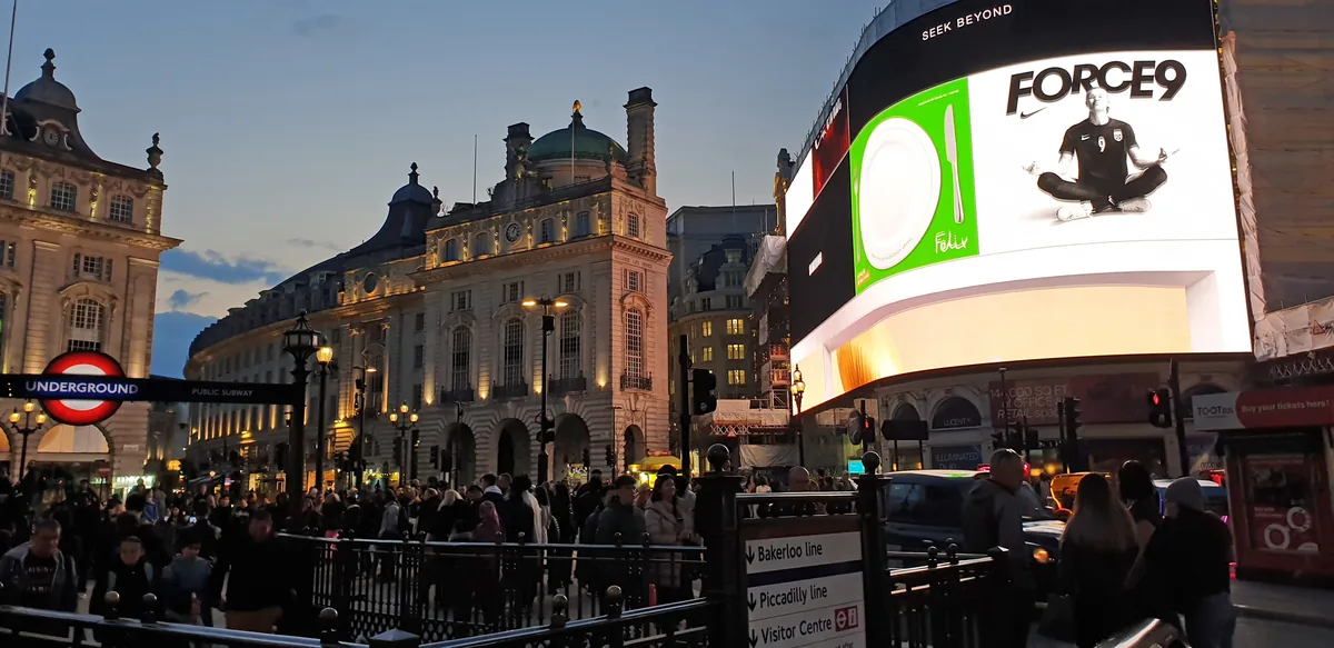 Crowds and lit screens at Piccadilly Circus in London at dusk
